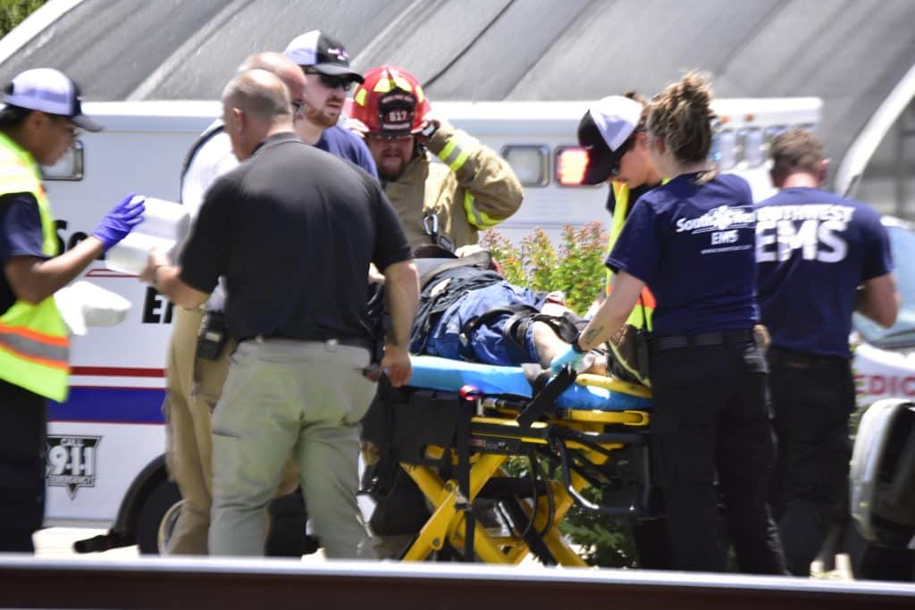 Emergency responders carry a patient on a wheeled stretcher toward an ambulance