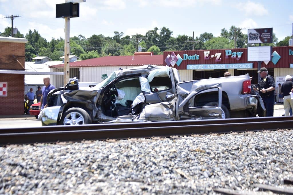 Two heavily damaged vehicles crash near a storefront with bystanders and a police officer inspecting the scene