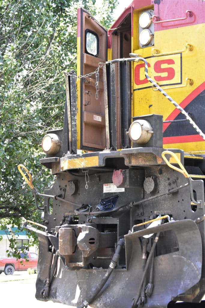 Front view of an old yellow red locomotive with an open cab door and visible safety chains