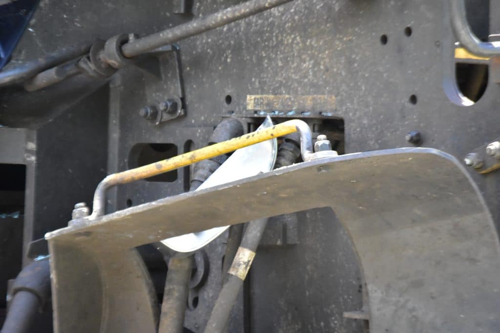 Close up of dusty industrial machinery with hoses bolts and metal brackets a yellow rod runs across the center of the frame
